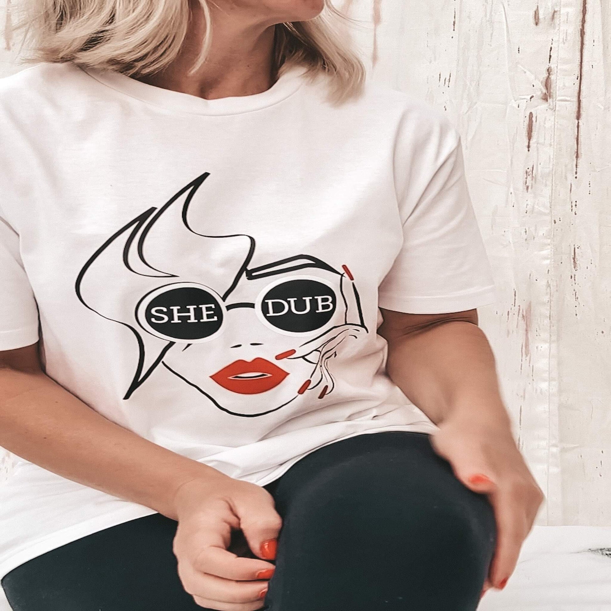 White T shirt with Shedub logo, line art ladies face with shedub round sunglasses, red lips and red finger nails. stand out.